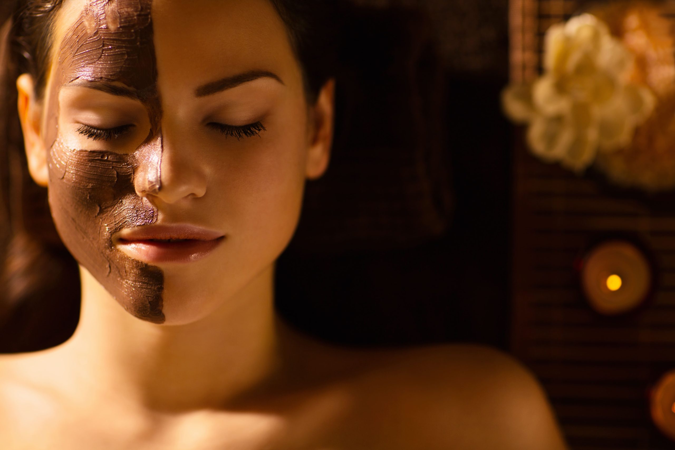 Mujer relajándose en un spa con una mascarilla facial aplicada en medio rostro, en un ambiente cálido con iluminación suave.